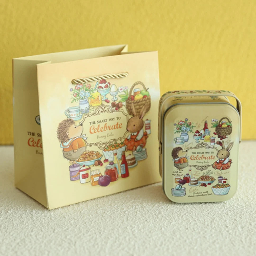 A light yellow tinplate candy box with a carrying loop featuring illustrations of treats and festive items.