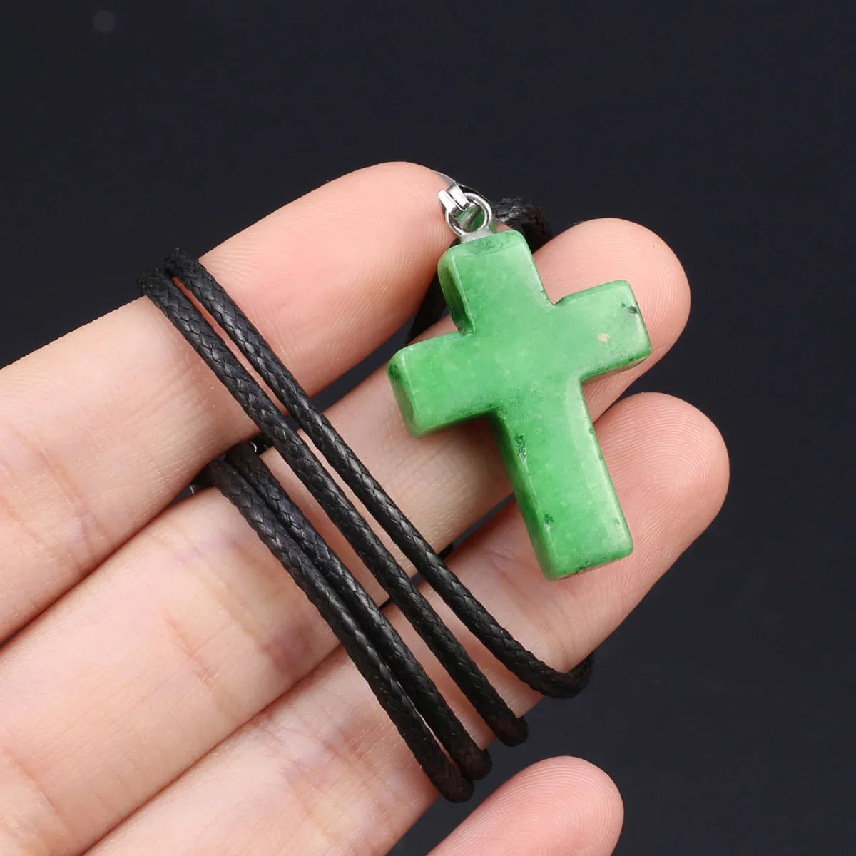 Eine Hand hält eine grüne Tigerauge-Agat-Kreuz-Anhängerkette mit schwarzem Schnur.