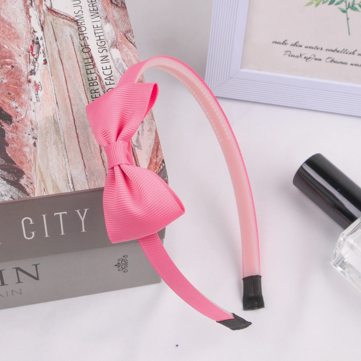 Pink grosgrain ribbon hair bow with black trim displayed next to a book and a picture frame.