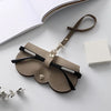 A tan leather pouch with a black strap and silver hardware is shown next to a white box.