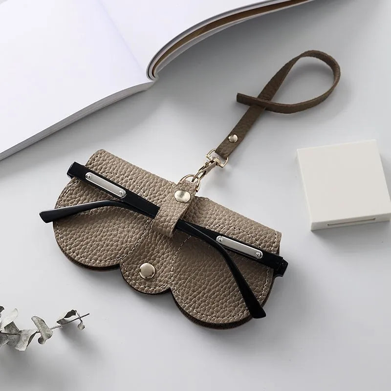 A tan leather pouch with a black strap and silver hardware is shown next to a white box.