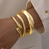 A close-up of a hand wearing a three-piece gold geometric wave bangle set.