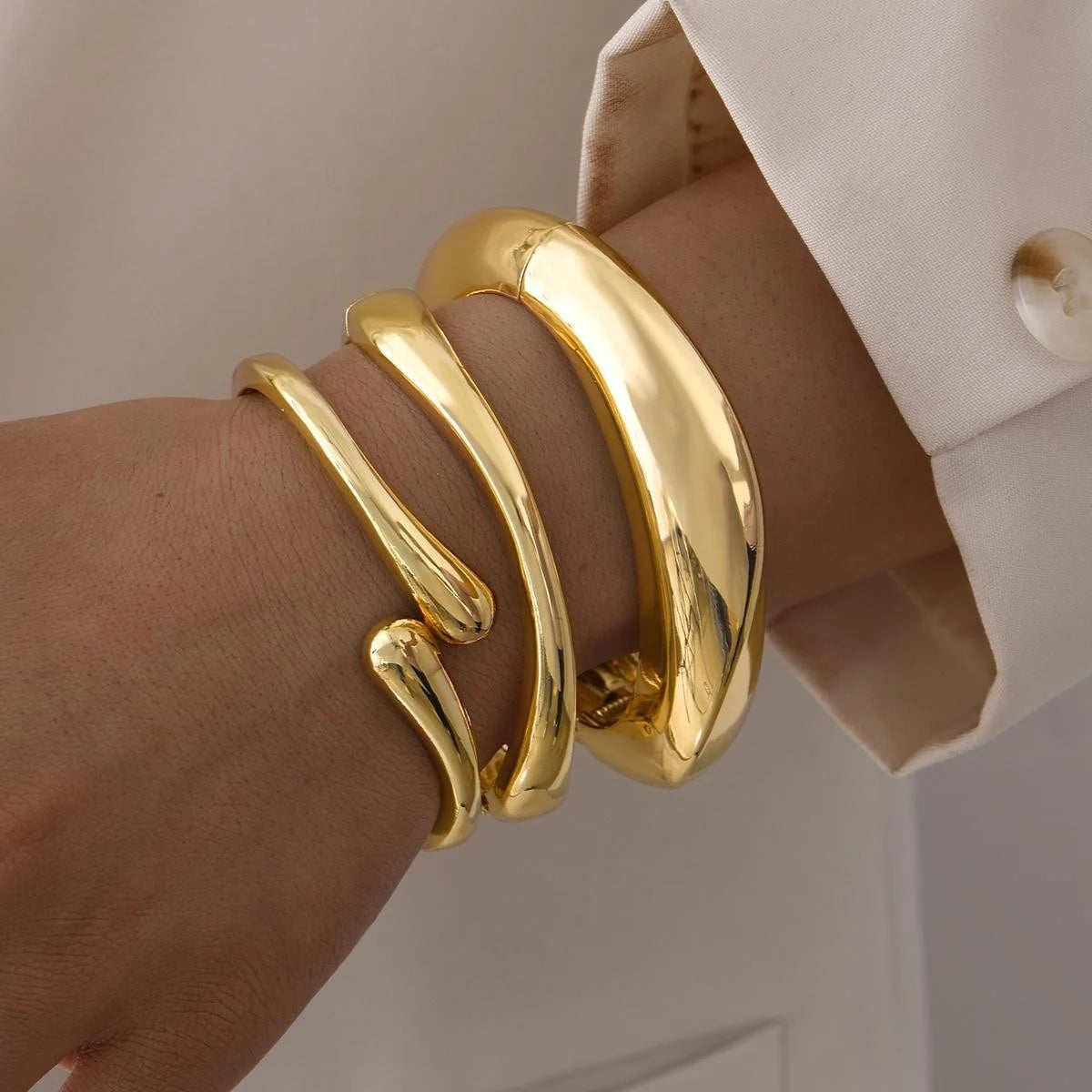 A close-up of a hand wearing a three-piece gold geometric wave bangle set.