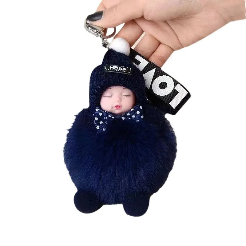 A dark blue fluffy plush doll with a hood and bow is being held by a hand, attached to a keychain.