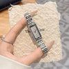 A close-up shot of a vintage gold stainless steel quartz watch worn on a finger, resting on a beige textured surface.