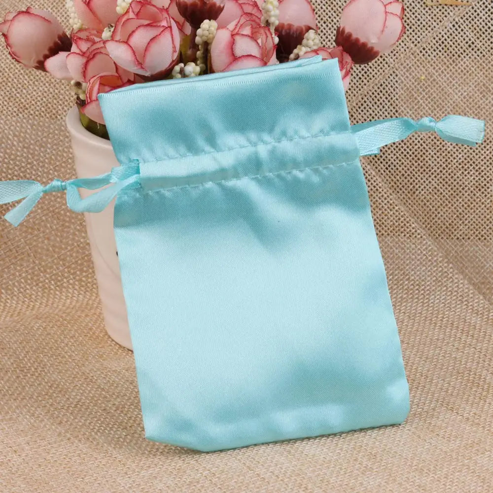 Light blue satin drawstring pouch with pink floral accents resting on burlap fabric.