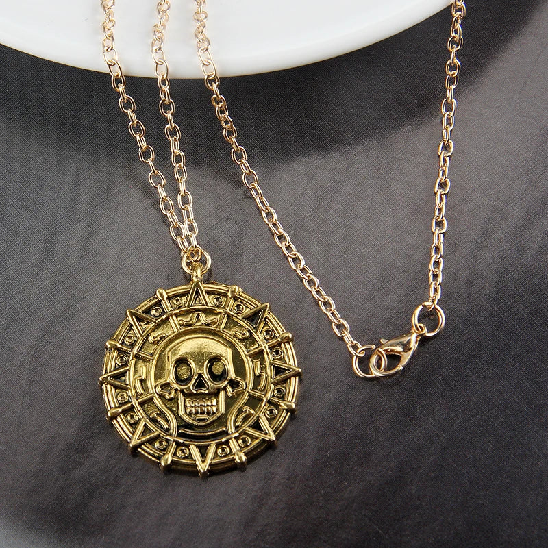 A gold-toned skull pendant necklace with a chain is displayed on a dark surface.