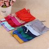 A collection of satin drawstring pouches in various colors, including red, pink, purple, blue, and green, laid out on a beige