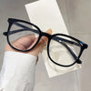 A hand holds a pair of black-framed anti-blue light spectacles against a white background.