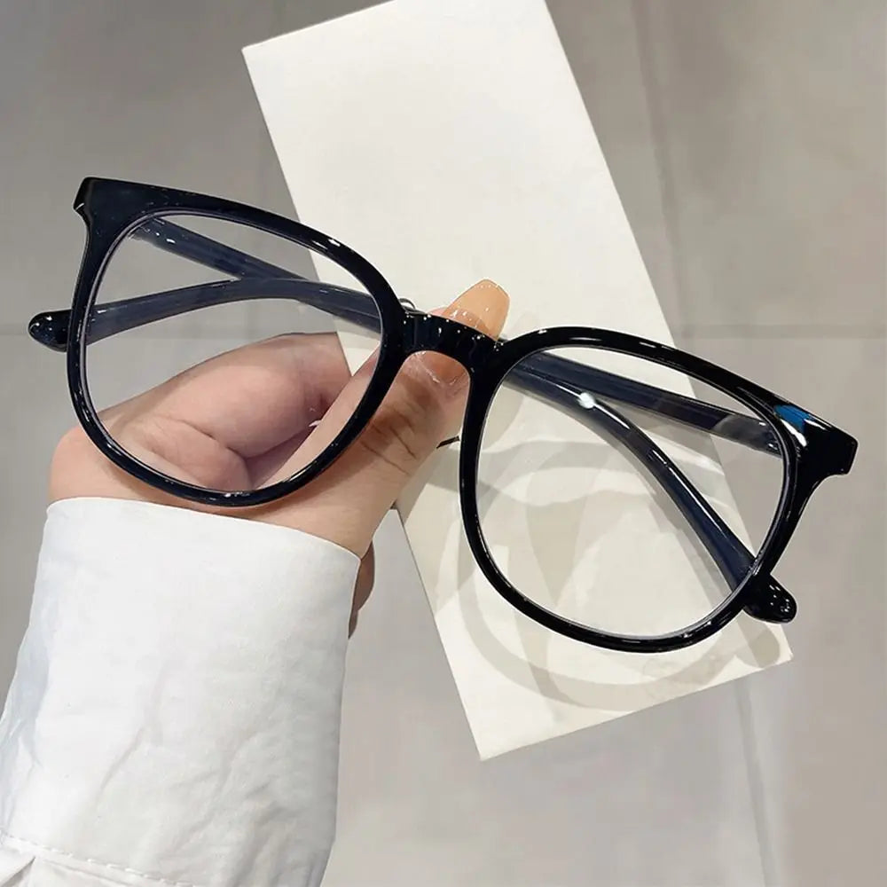 A hand holds a pair of black-framed anti-blue light spectacles against a white background.