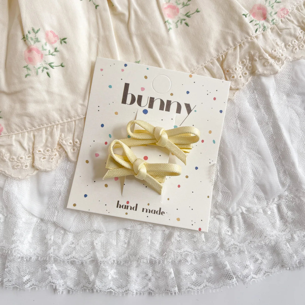 Un ensemble de pinces à cheveux en nœud jaune faites à la main, présentées sur une carte sur un fond de tissu blanc.
