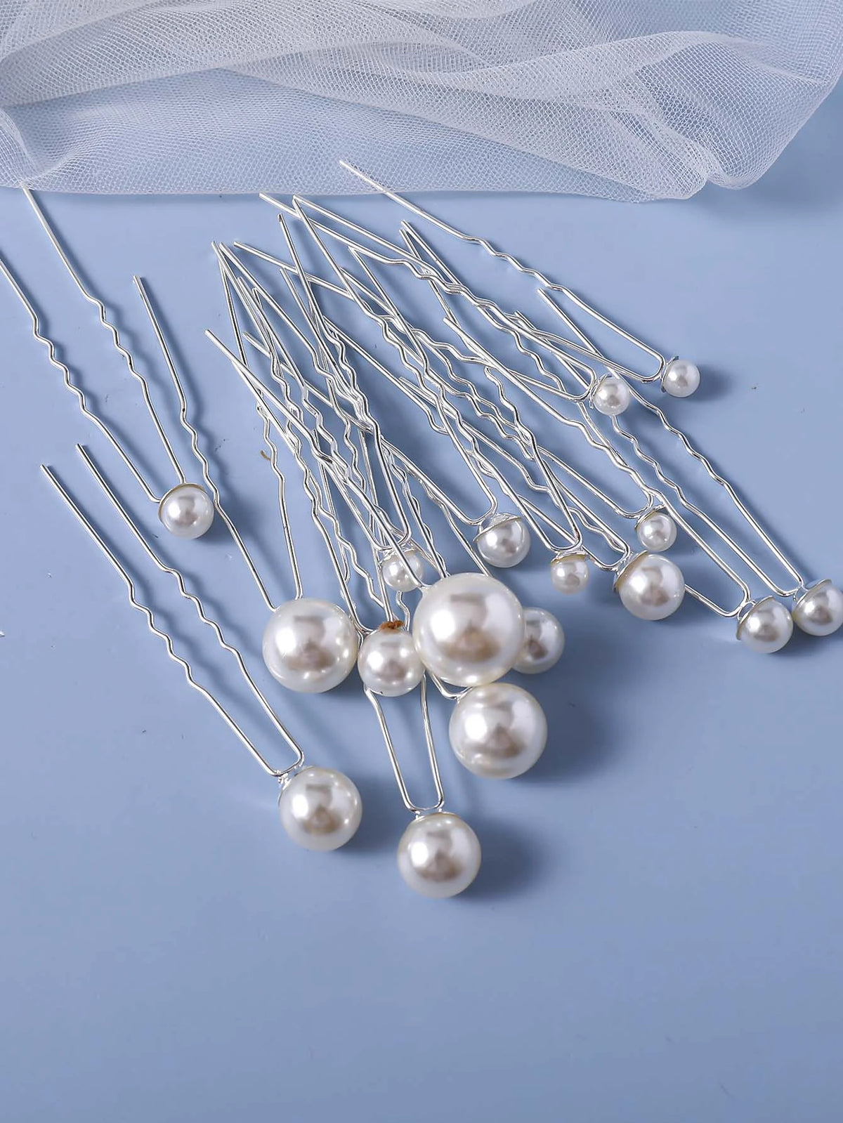 A collection of 18 faux pearl hair pins with silver wires arranged on a light blue surface.