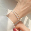 A close-up of a Sterling Silver double heart charm bracelet worn on a wrist against a bright, sunlit background.
