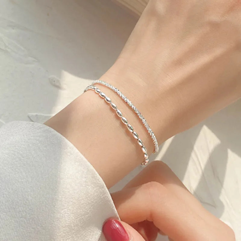 A close-up of a Sterling Silver double heart charm bracelet worn on a wrist against a bright, sunlit background.