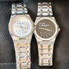 A pair of stainless steel octagonal watches with a slogan dial resting on a dark surface.
