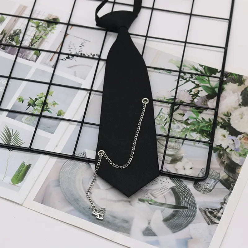 A black classic chain necktie accessory with a silver chain and charm displayed on a grid background.