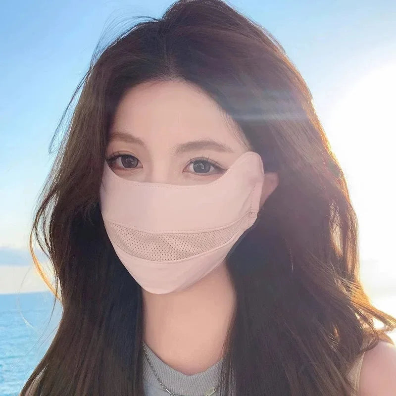 A woman wearing a light pink breathable ice silk UV protection face mask against a bright sky and ocean background.