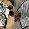 A black and white floral print silk scarf draped on a beige blazer and displayed next to a folded scarf.