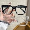 A hand holds a pair of black geometric reading glasses with transparent lenses.