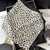 A black and beige leopard print silk scarf is displayed in a dark frame on a black surface.