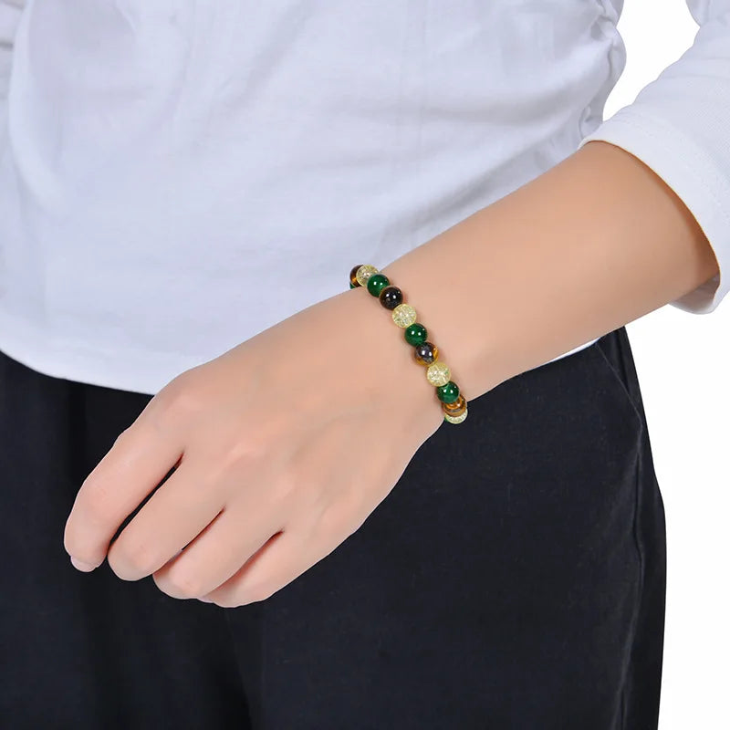 A close-up of a hand wearing a Tiger Eye crystal bracelet with green and gold beads.