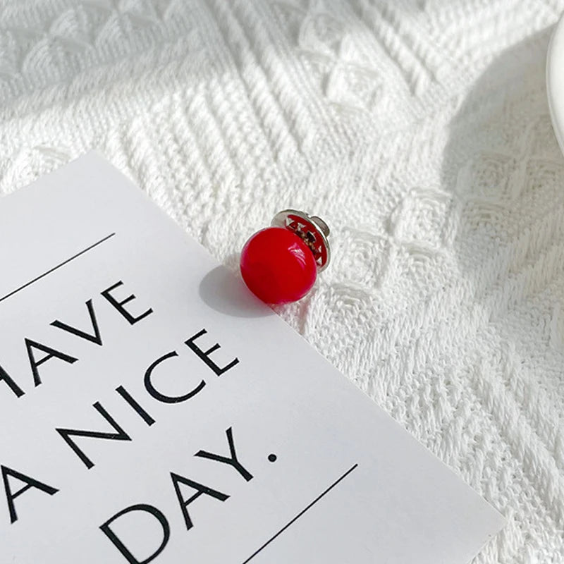 A bright red pearl button set resting on a white card against a textured white fabric background.