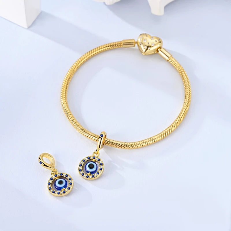 Gold charm bracelet with a heart pendant and a devil's eye charm on a white background