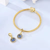 Gold charm bracelet with a heart pendant and a devil's eye charm on a white background