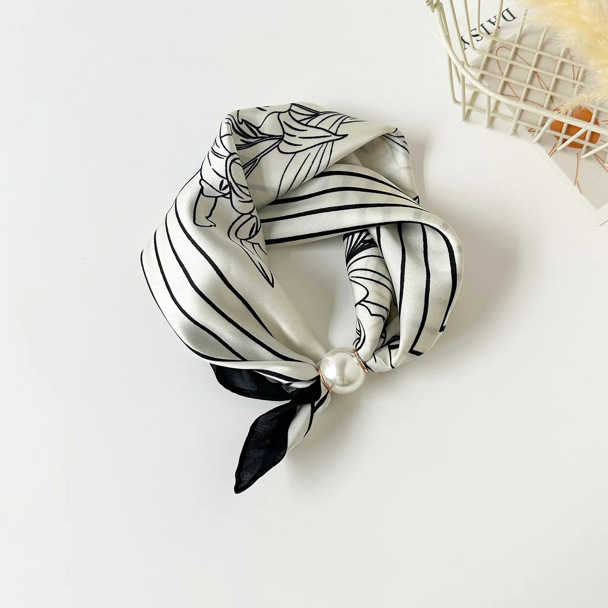 A silk scarf featuring a black and white floral print tied in a bow with a pearl accent.