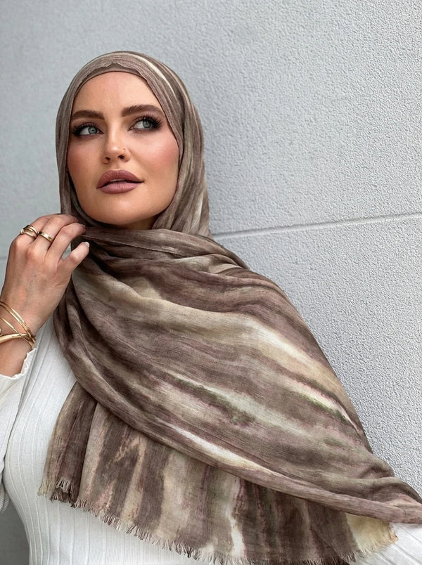 امرأة ترتدي وشاح حجاب من القطن الرايون مخطط باللونين البني والبيج ومتدلى حول عنقها.