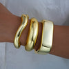 A set of three gold geometric wave bangles worn on a wrist.