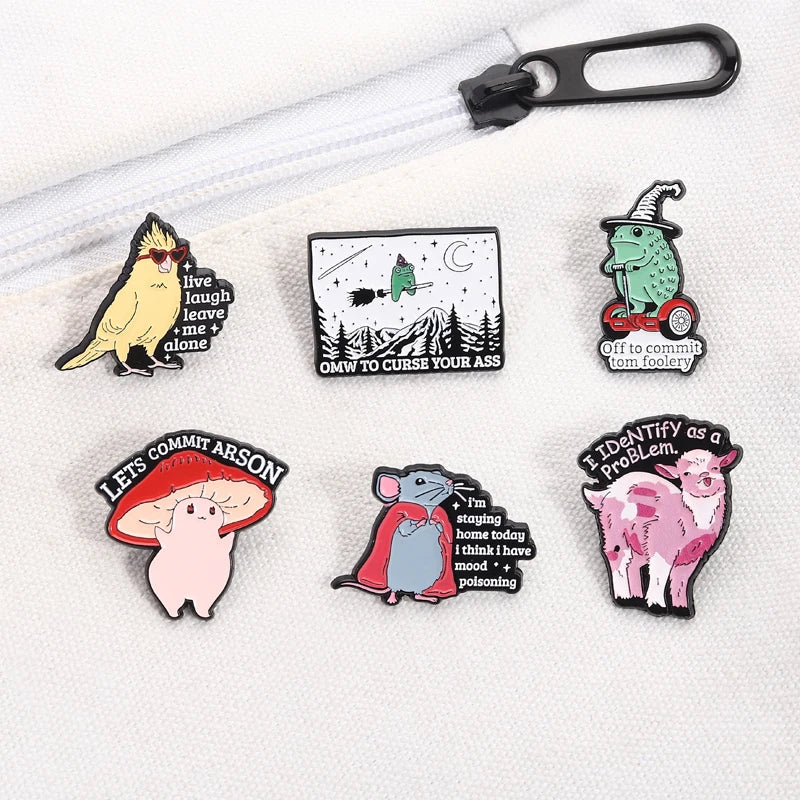 A collection of enamel pins featuring whimsical characters and phrases like a yellow bird, a witch, and a pig.