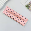 A pink fabric headband with small navy blue polka dots lying on a light gray surface.