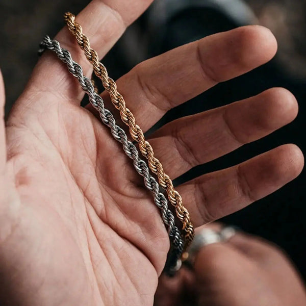 A hand holds a twisted rope necklace made of gold and silver-toned metal.