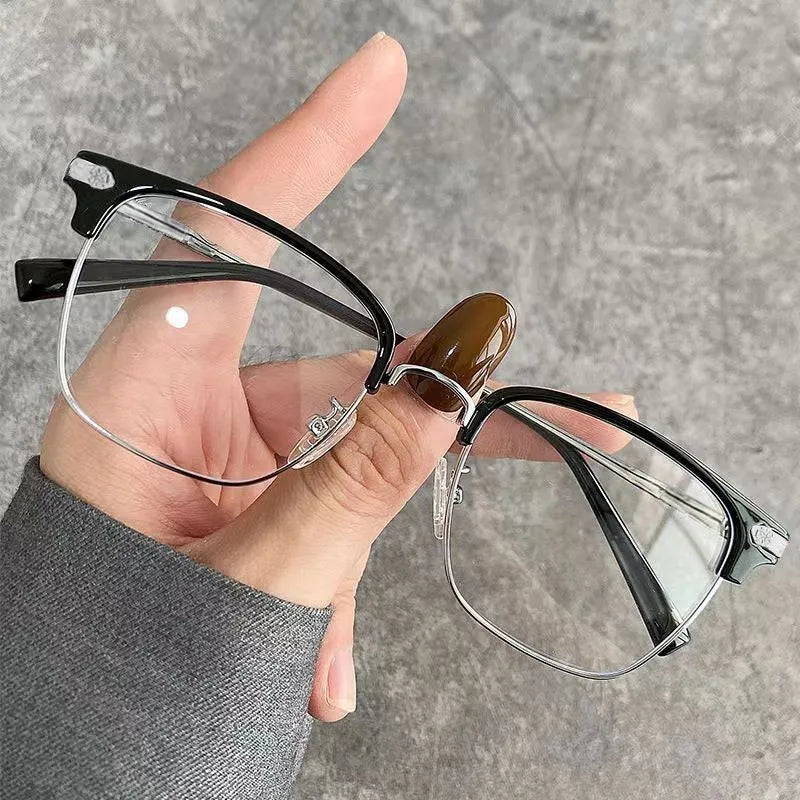 A hand holds a pair of black and brown fashion metal half-frame reading glasses against a gray background.