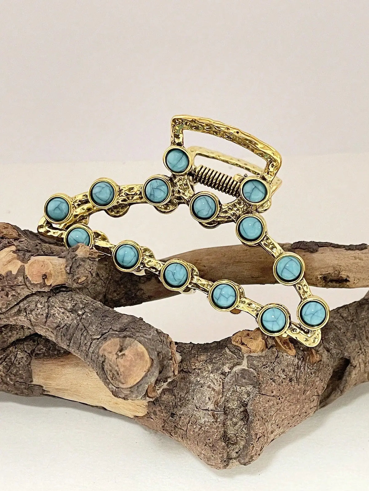 Gold metal hair claw clips decorated with light blue turquoise beads resting on a piece of driftwood.