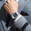 A hand wearing a silver stainless steel quartz watch is adjusting the cuff of a gray suit jacket.