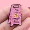 Pin de esmalte rosa con un triángulo de precaución amarillo y el texto: 'No estoy de humor, acérquese con precaución'.