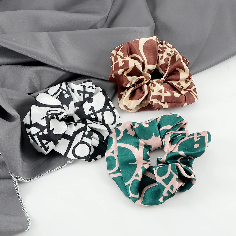 Three colorful knitted hair scrunchie headbands in brown, beige, and green patterns displayed on a gray fabric.