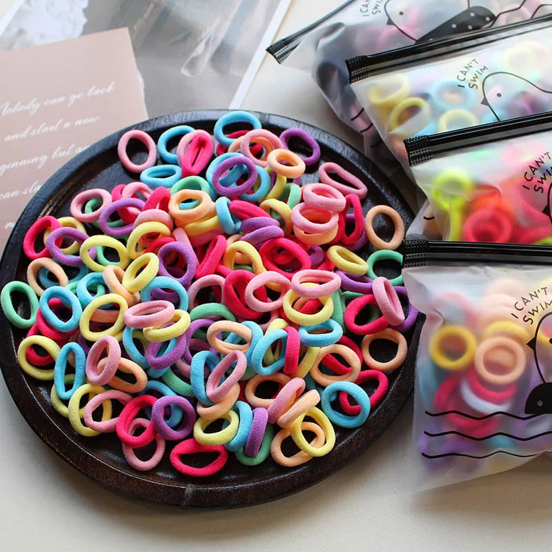 A pile of colorful elastic hair bands in various shades of pink, purple, yellow, and blue are displayed on a dark plate.