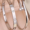 A pair of silver stainless steel bracelets featuring four-leaf clover and nail charms.
