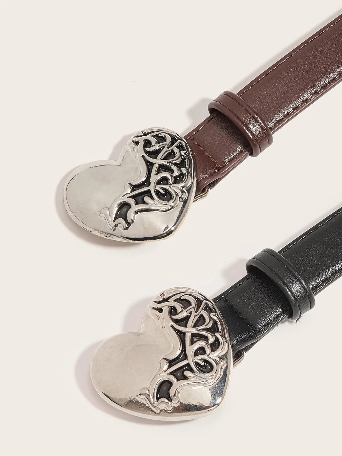 Primer plano de un cinturón de cierre de corazón metálico vintage con diseño ornamentado y correa de cuero marrón.
