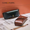 Estuche suave retro verde oscuro de PU para gafas y joyas sobre una superficie de mármol.