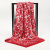 A vibrant red silk scarf featuring a detailed white floral pattern displayed on a black hanger.