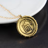 A gold skull pendant necklace with a geometric design rests on a white plate.