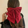 A close-up of a large red satin bow hair clip tied in a bow on a person's hair.