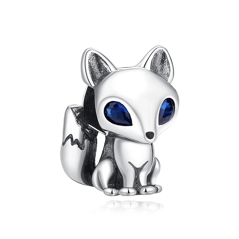 A silver charm of a fox head with blue eyes and a tree silhouette detail.