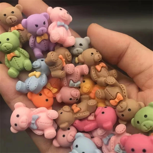 Eine Hand hält eine Sammlung von 10 rosa und beigeen Harz-Nagelkunst-Charms mit niedlichen Bären- und Tierfiguren.