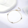 A delicate gold-plated ankle bracelet featuring small blue gemstones and a chain, displayed on a white surface.