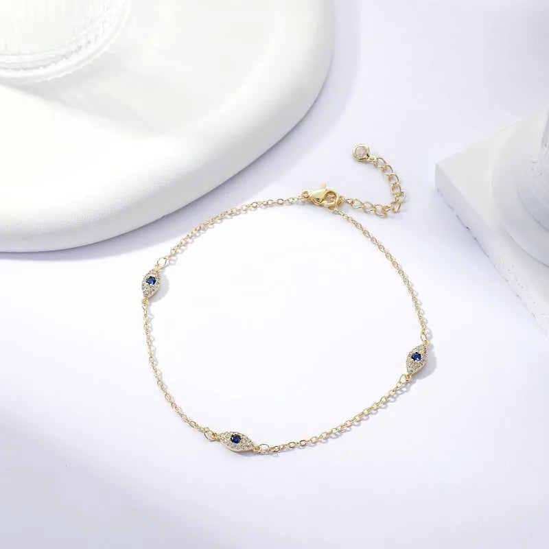 A delicate gold-plated ankle bracelet featuring small blue gemstones and a chain, displayed on a white surface.